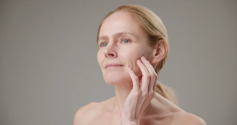 A woman with mature skin gently touching her cheek, showcasing the care and attention given to aging skin.