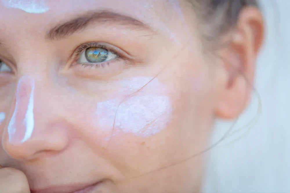A close-up of a woman applying moisturiser with SPF to her face, with a small amount of product visible on her skin.