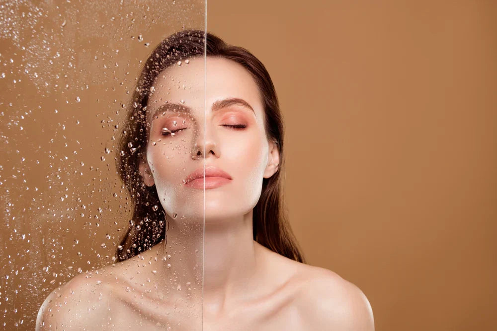 A woman with glowing skin, standing behind a glass pane with water droplets, looking serene and refreshed, representing the 'glass skin' skincare trend.