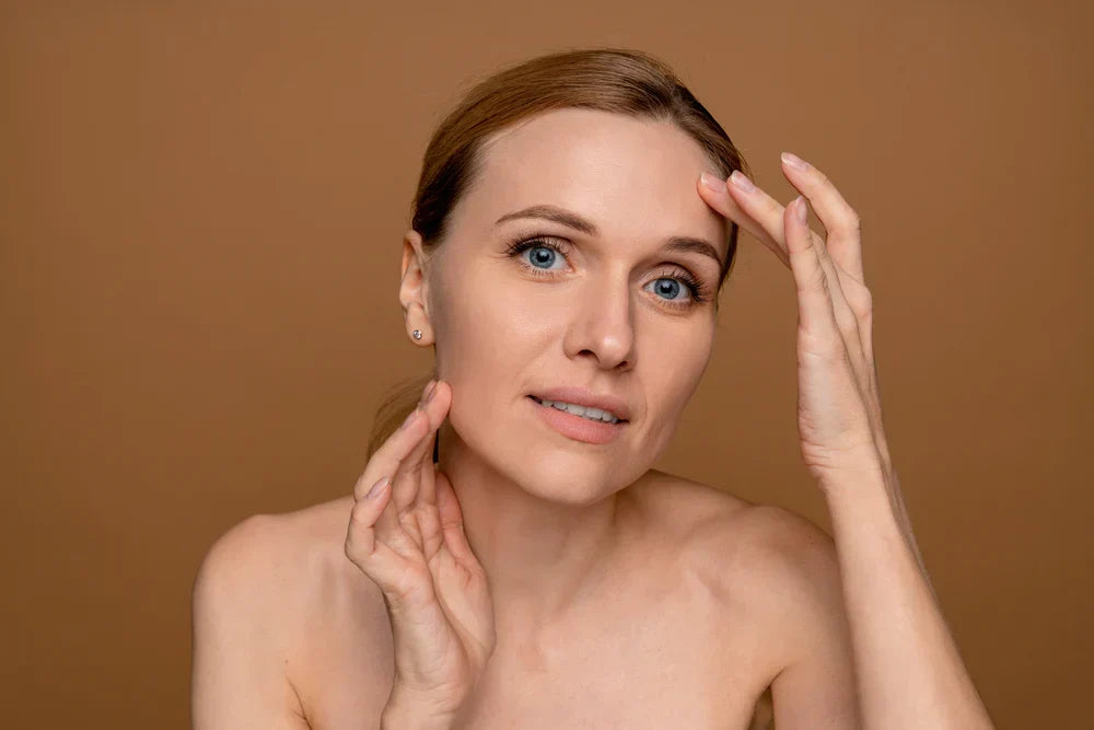 A woman gently touching her face, focusing on her forehead and jawline, with a somewhat concerned expression, highlighting skincare for aging skin.
