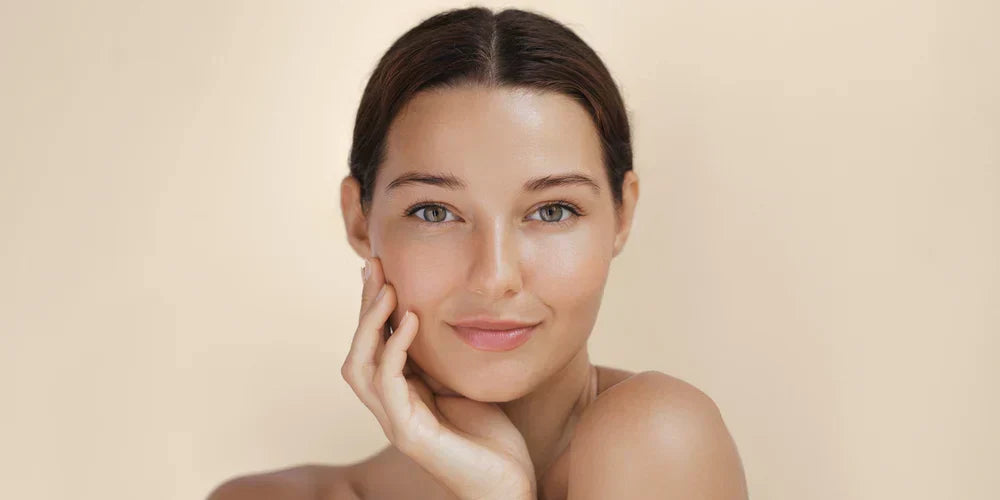 A woman with smooth, glowing skin gently touching her face, smiling softly, suggesting the use of a gentle cleanser for healthy skin.