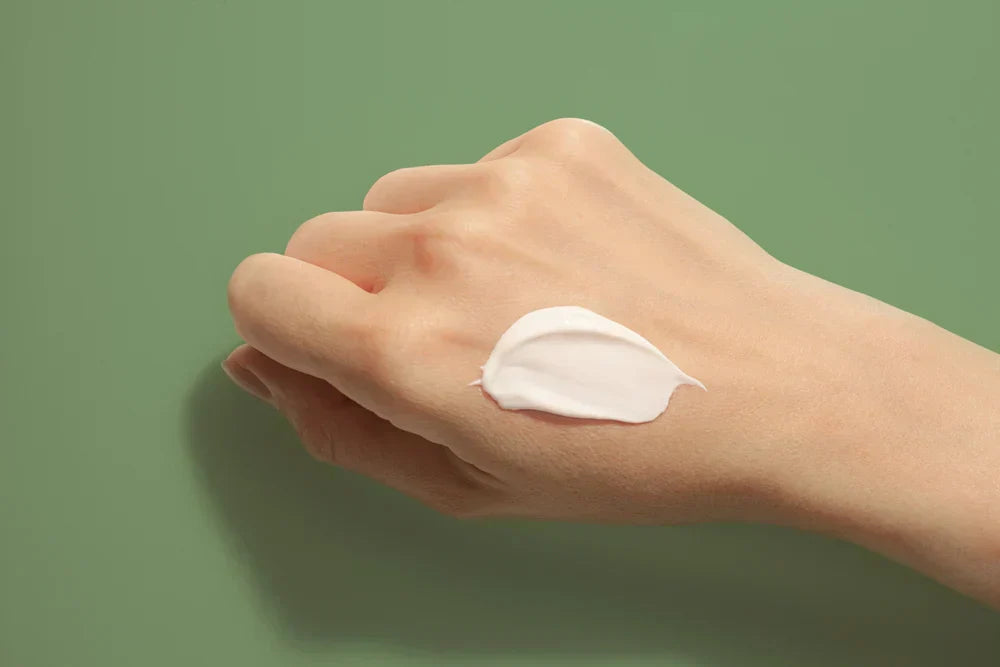 A hand with a small amount of balm cleanser applied to the skin, showcasing its smooth, creamy texture against a green background.